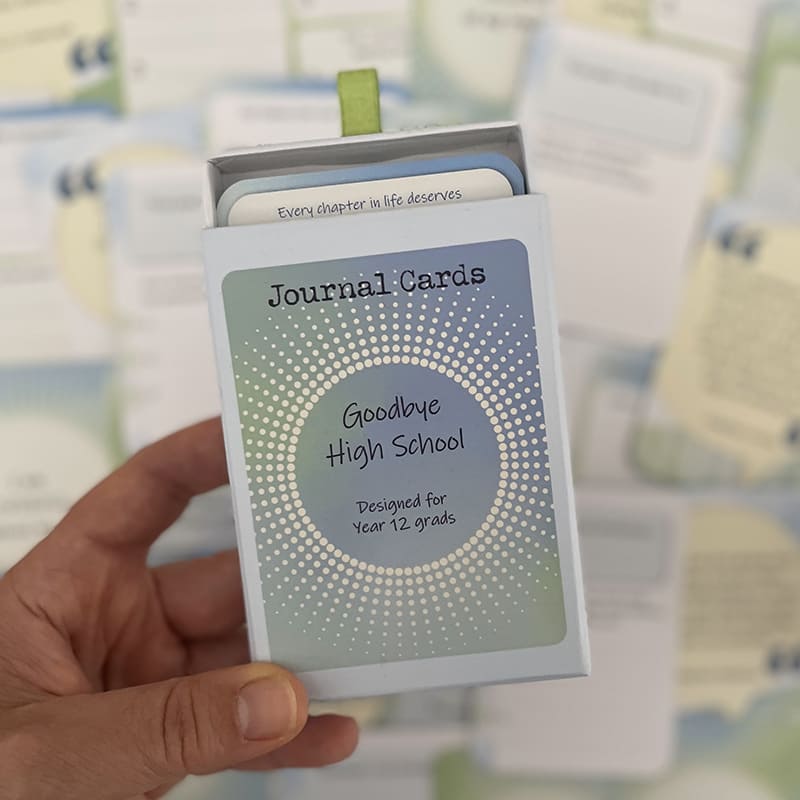 Goodbye High School Journal Cards – deck for Year 12 grads, open box held in hand with prompt cards reading "Every chapter in life deserves..." visible inside.