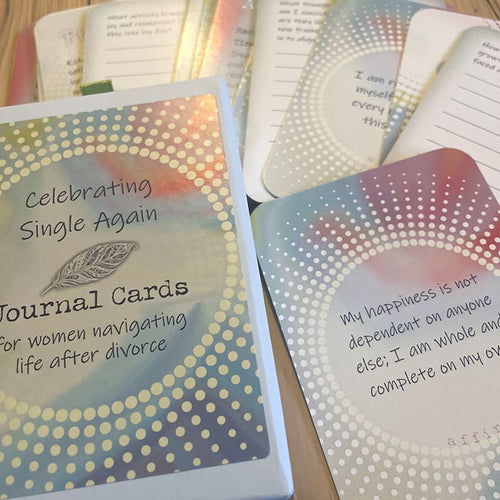 The closed card box beside a card reading "My happiness is not dependent on anyone else; I am whole and complete on my own – affirmation," with other prompt and affirmation cards fanned out behind it.